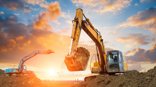 Zwei Bagger arbeiten im frühen Morgenlicht auf einer Baustelle