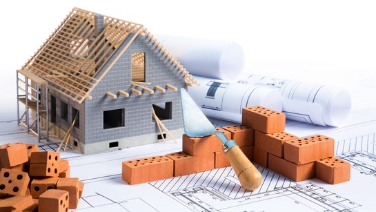 Ein Bauplan mit Modellhaus und Maurerkelle